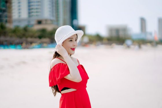 Girl with red dress and white hat on beach.